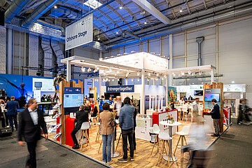 Messestand auf der WindEnergy Hamburg mit Besucherinnen und Besuchern im Gesprächs- und Networkingbereich. Über dem Stand hängt ein Schild mit der Aufschrift „Offshore Stage“. Der offen gestaltete Ausstellungsbereich mit Sitzgelegenheiten, Informationsdisplays und Exponaten zeigt die lebhafte Atmosphäre der Fachmesse.