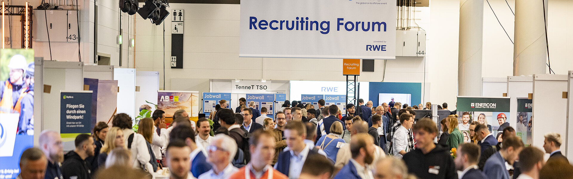 View over the crowd to the recruiting area. A large sign hanging from the ceiling reads Recruiting Forum.