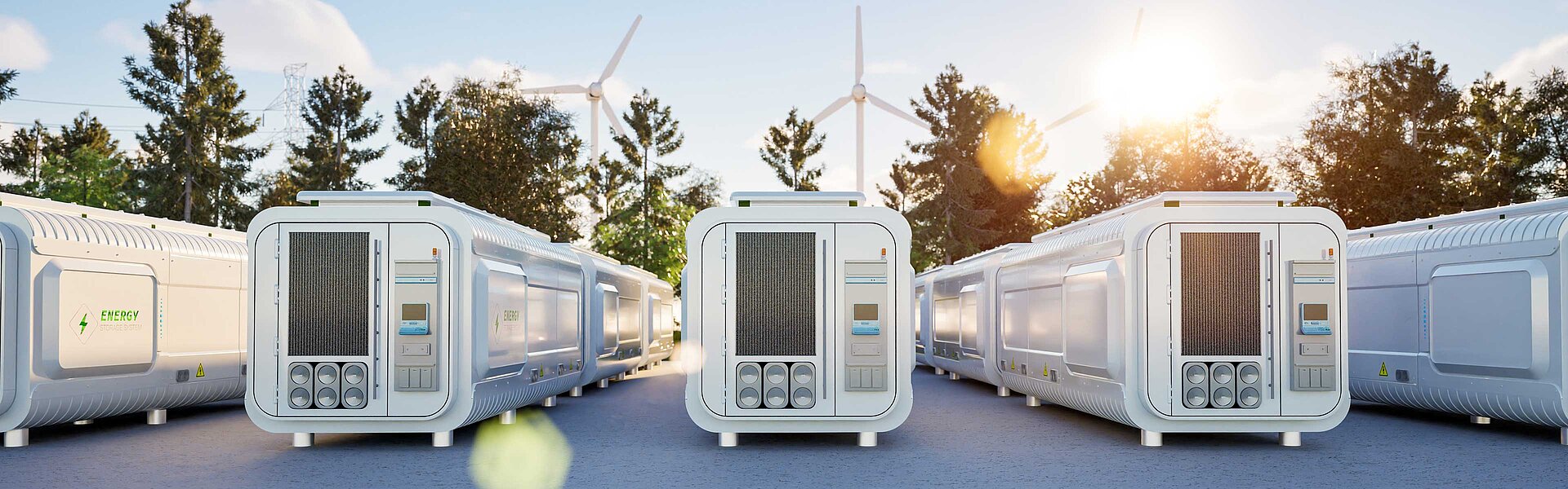 Several energy storage units are lined up next to each other. Behind the containers, blue skies and wind turbines can be seen.