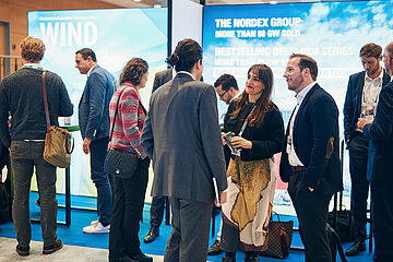 Networking-Bereich auf einer Windenergie-Messe mit Personen im Gespräch vor einem Stand der Nordex Group.