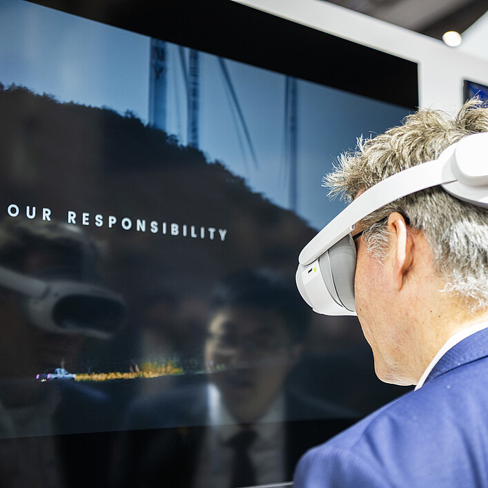 Person nutzt eine Virtual-Reality-Brille vor einem Bildschirm während einer Messepräsentation.