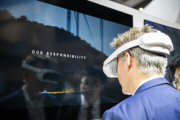 Person nutzt eine Virtual-Reality-Brille vor einem Bildschirm während einer Messepräsentation.