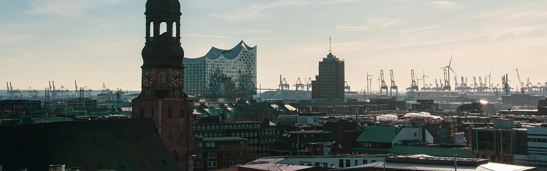 Key visual of the RECHARGE Wind Power Summit. View of the main church St. Michaelis, the Elbphilharmonie concert hall and Hamburg harbour. Wind turbines can be seen in the background.