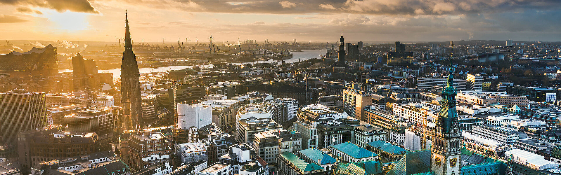 Key visual of the RECHARGE WindPower Summit. View of Hamburg with St. Michael's Church, the Elbphilharmonie, the Port of Hamburg, and City Hall. Wind turbines can be seen in the background.