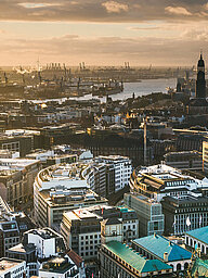 Key visual of the RECHARGE WindPower Summit. View of Hamburg with St. Michael's Church, the Elbphilharmonie, the Port of Hamburg, and City Hall. Wind turbines can be seen in the background.